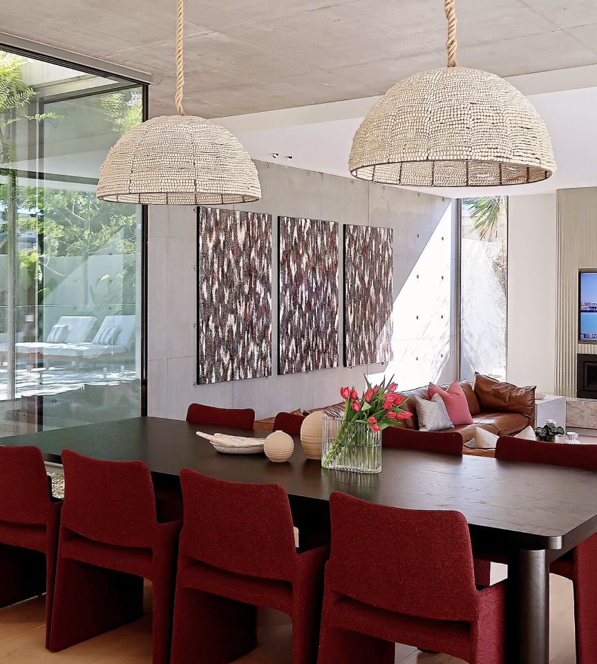 Modern Melbourne mansion dining room with Wilson Lin's art, wooden table, red chairs, pendant lights, and tulips